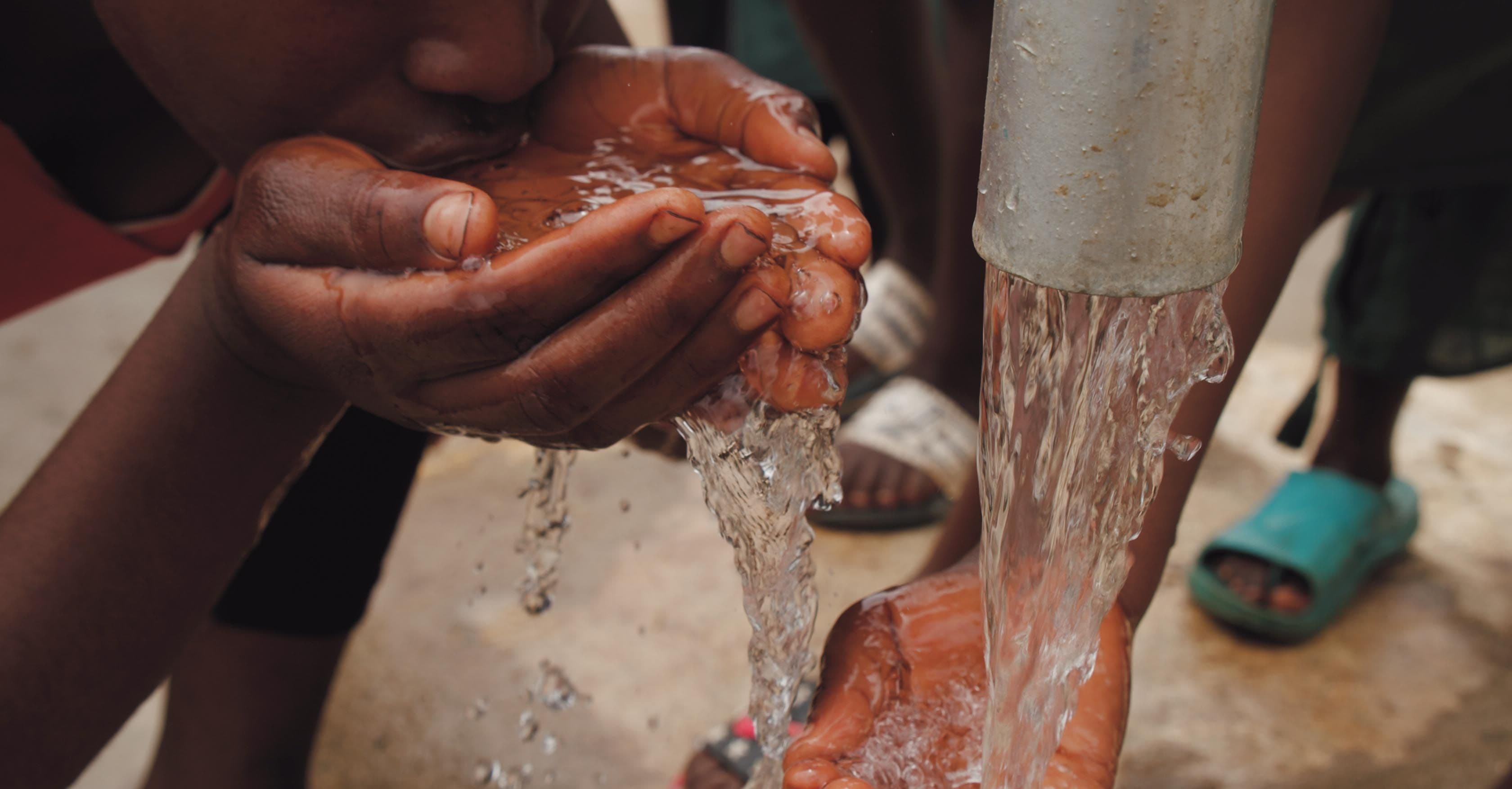 Child drinking clean water from cupped hands at a communal tap